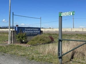 The blue Central Valley Christian School sign next to a green street sign that says Andrew Lane next toa highway.